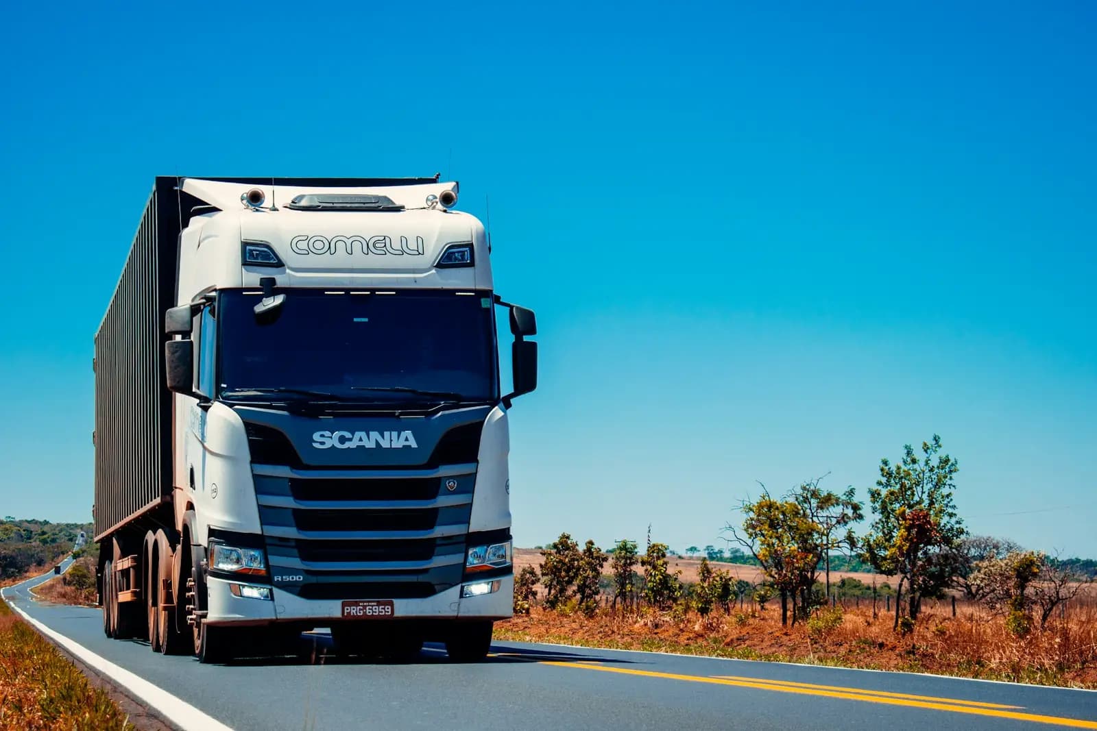 Kuru bir otoyolda seyreden beyaz Scania çekici ve kapalı dorsesi